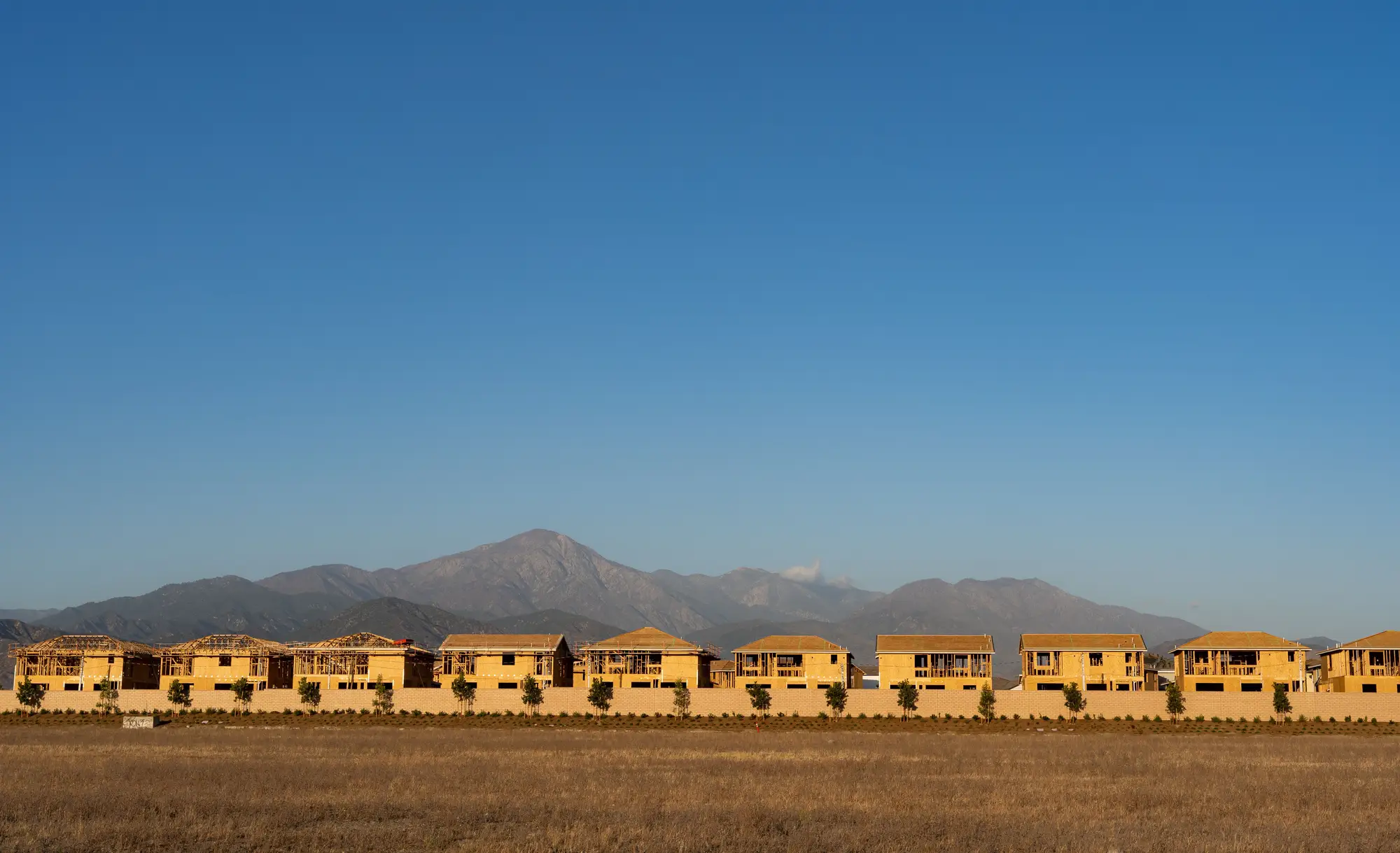 A row of half-built timber-frame houses on open ground, with mountains behind